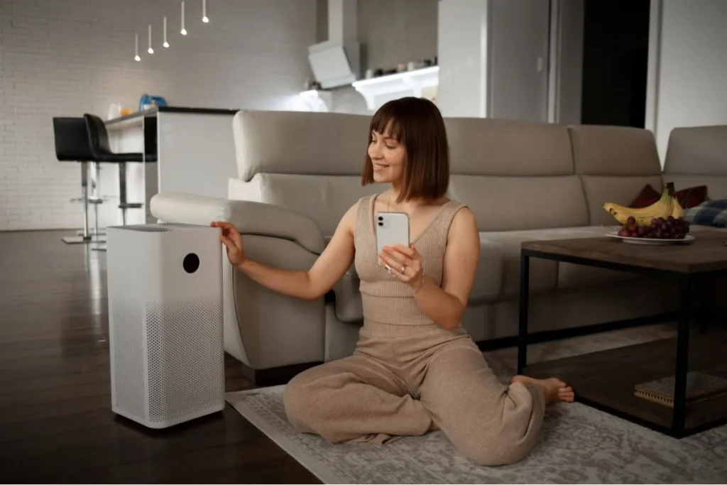 Happy woman sitting beside air purifier, indicating clean and fresh indoor air quality.